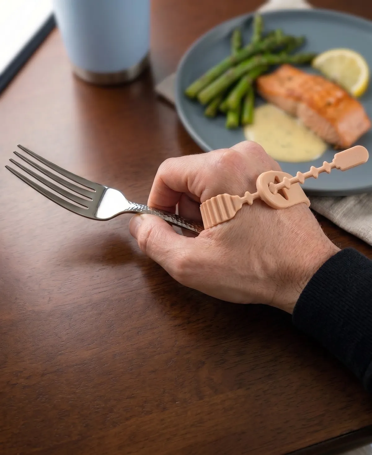 A hand wearing the OmniWrap Assist holding a fork over a dinner plate
